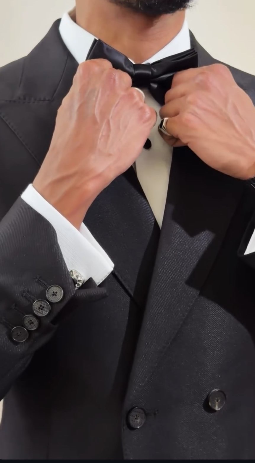 Groom adjusting a black silk bow tie on a double-breasted tuxedo
