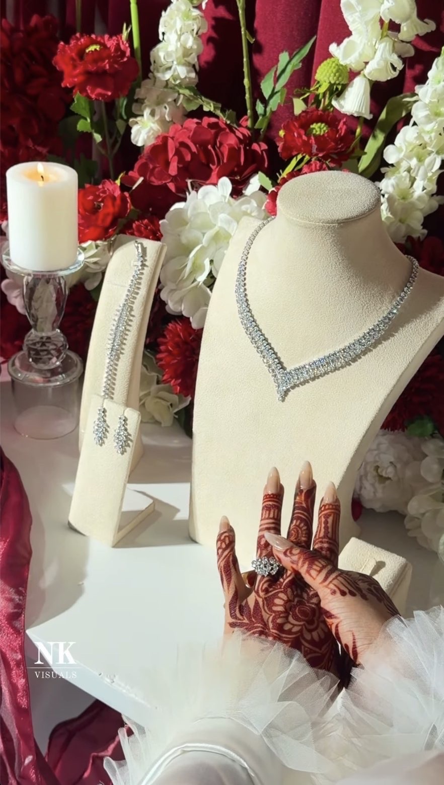 Silver necklace and earrings on ivory stands with a henna-painted hand and red florals