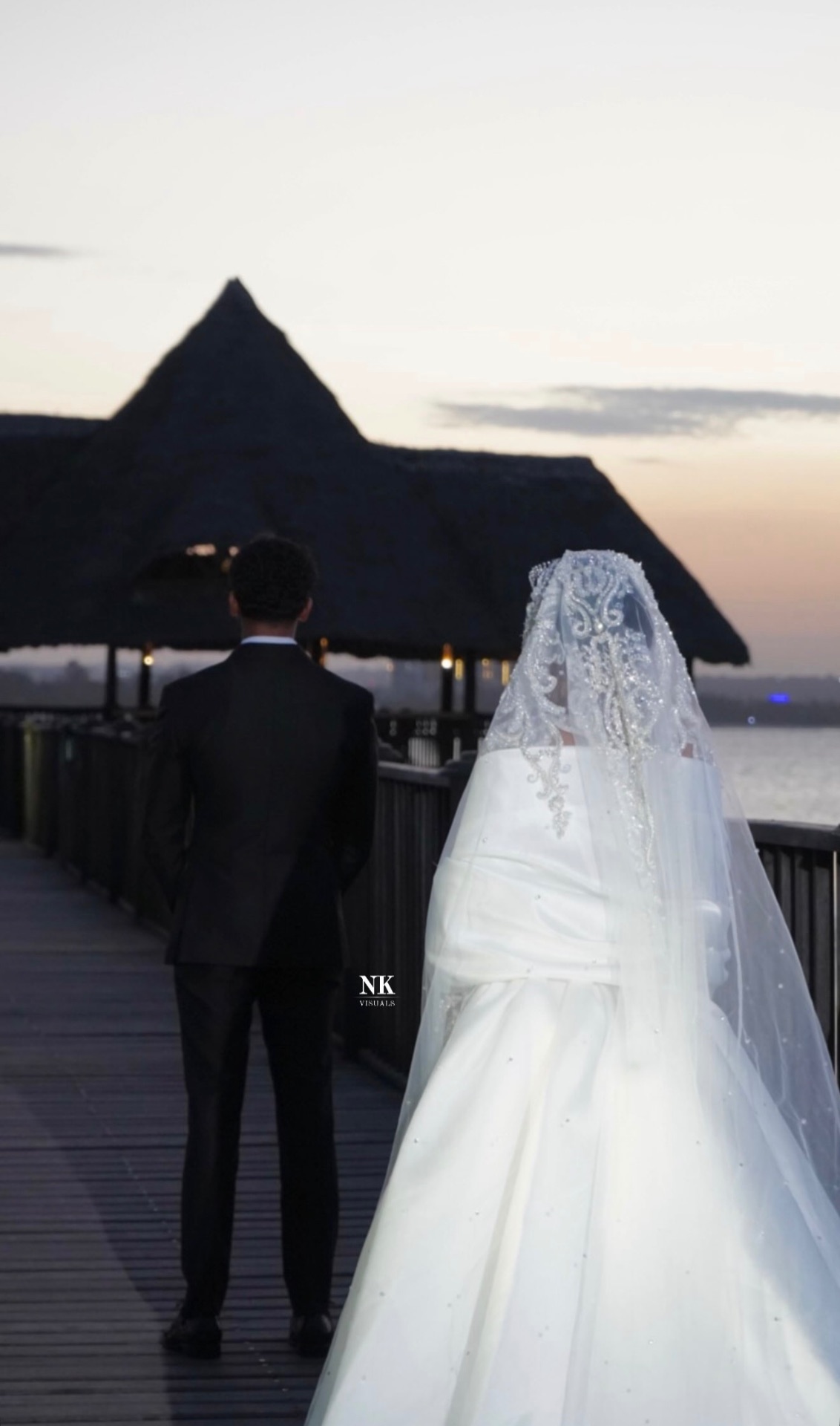 Bride and groom on a wooden pier at sunset, seen from behind