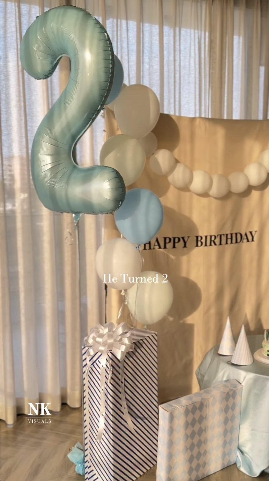 Second birthday setup with a pale blue number 2 balloon, garland and wrapped gifts
